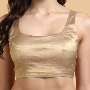 Puede incluir: Una blusa dorada sin mangas con cuello redondo. La tela tiene un brillo sutil y la prenda parece estar hecha a medida. La blusa es de color liso y adecuada para diversas ocasiones.