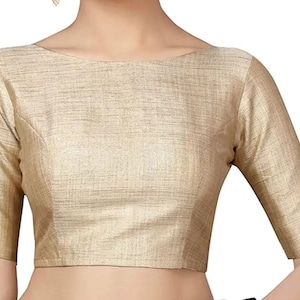 May include: A gold-colored blouse with a boat neckline and three-quarter sleeves. The fabric has a subtle textured appearance. The blouse is a solid color and appears to be made of a lightweight material.