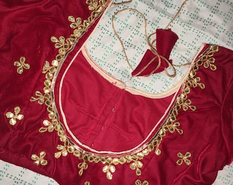 May include: A red velvet blouse with gold embroidery and embellishments. The blouse has a round neckline and a hook and eye closure at the back.