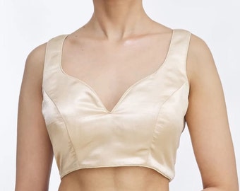 May include: A sleeveless, satin, cream-colored, scoop-neck top.