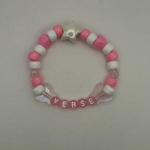 May include: A beaded bracelet featuring alternating pink and white round beads, a single iridescent star-shaped bead at the top, and two translucent butterfly-shaped beads flanking the word VERSE spelled out in white letters on pink beads.