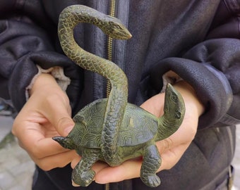 May include: A bronze sculpture of a turtle with a snake wrapped around it. The turtle has a detailed shell pattern, and the snake is coiled around the turtle's body. The sculpture has a weathered, antique appearance.