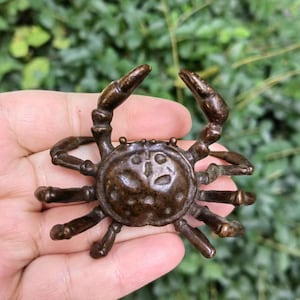 Puede incluir: Figura de cangrejo de bronce con pinzas y patas detalladas. El cangrejo tiene una superficie texturizada y está posado con las pinzas levantadas. La figura es un objeto decorativo, probablemente para exhibición o colección.