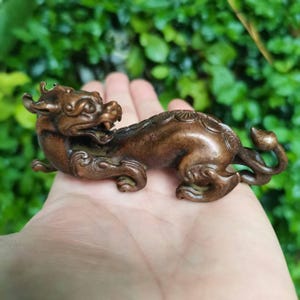 May include: A bronze-colored figurine of a mythical creature, possibly a dragon or a similar beast. The sculpture has intricate details, including horns, scales, and a curled tail. The figure is lying down, with its front paws extended.