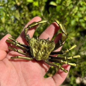 Puede incluir: Figurilla de cangrejo detallada de estilo antiguo, con acabado dorado metálico. El cangrejo tiene detalles intrincados en su caparazón y patas, con una superficie texturizada. Un artículo decorativo, posiblemente un objeto de colección de temática náutica.