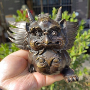May include: Bronze-coloured mythical creature figurine with detailed wings, horns, and a fierce expression. The sculpture has intricate detailing and a weathered finish, suggesting an antique or vintage piece. The creature is in a crouching position.