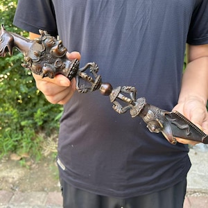 May include: A bronze ritual dagger with detailed carvings. The dagger features depictions of faces, animals, and ornate patterns. The handle and blade are connected by a central, decorative element.