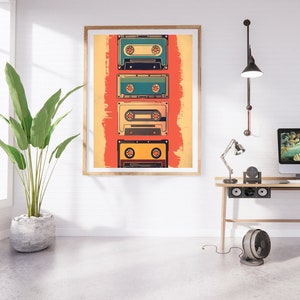 Op de afbeelding: Een ingelijst afdruk van vijf vintage cassettebandjes op een rode en gele achtergrond. De bandjes zijn verticaal gerangschikt en zijn allemaal in verschillende kleuren. De afdruk hangt aan een witte muur boven een houten bureau met een lamp, een computermonitor en een ventilator.