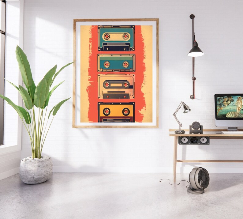 Op de afbeelding: Een ingelijst afdruk van vijf vintage cassettebandjes op een rode en gele achtergrond. De bandjes zijn verticaal gerangschikt en zijn allemaal in verschillende kleuren. De afdruk hangt aan een witte muur boven een houten bureau met een lamp, een computermonitor en een ventilator.