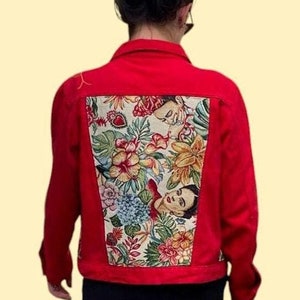Puede incluir: Una chaqueta vaquera roja con un diseño floral y un retrato en la espalda. El diseño presenta el rostro de una mujer y flores en tonos amarillos, verdes, azules y rosas.