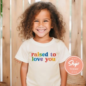 a little girl wearing a t - shirt that says raised to love you