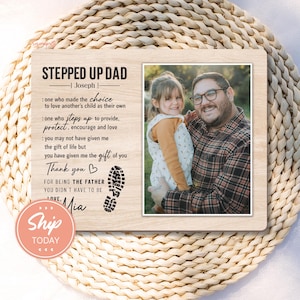 May include: Wooden photo frame with a picture of a man and a child. The frame has text that reads "STEPPED UP DAD" and a message of appreciation. The frame also has a footprint graphic and the words "Thank you" and "Love".