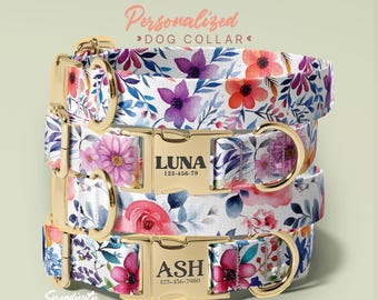 May include: Stacked personalized dog collars with floral patterns in purple, red, and pink. Each collar has a gold-colored buckle with a name and phone number. The collars are white with blue and green leaves.