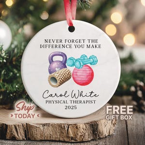May include: A white ceramic Christmas ornament with a red ribbon. The ornament features a purple kettlebell, blue dumbbells, a foam roller, and a pink exercise ball. Text reads "NEVER FORGET THE DIFFERENCE YOU MAKE" and "Carol White, PHYSICAL THERAPIST 2025."