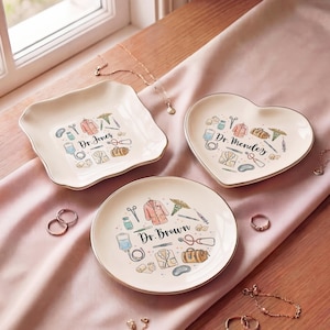 May include: Three decorative ceramic trays with gold rims, each featuring a different shape and design. The trays are adorned with medical-themed illustrations and the names "Dr. Jones", "Dr. Mendez", and "Dr. Brown".