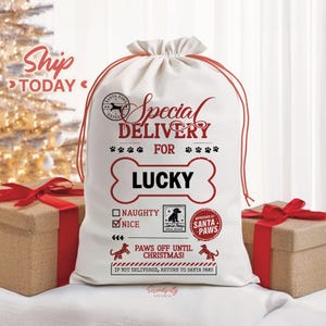 May include: A white canvas drawstring gift bag with red text that reads "Special Delivery For Lucky". The bag has a bone-shaped design and paw prints. The text "Nice" is checked. The bag is for Santa Paws.
