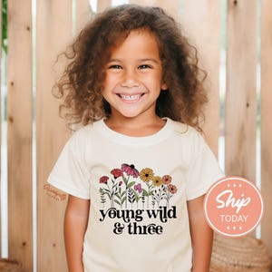 a young girl wearing a t - shirt that says young wild and three