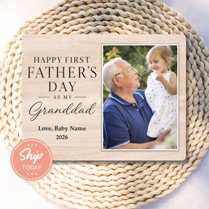 May include: A light wood-tone picture frame with the text "HAPPY FIRST FATHER'S DAY AS MY Granddad" and the year 2026. The frame holds a photo of a grandfather and grandchild. A pink "Ship Today" sticker is in the lower left corner.