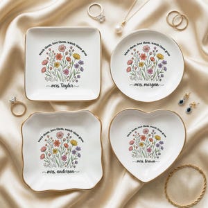 May include: Four white ceramic ring dishes with gold trim, each featuring a floral design and the text "teach them, love them, watch them grow." The dishes are square, round, scalloped, and heart-shaped, with personalized names.