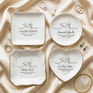 May include: Four white ceramic trinket dishes with gold rims, each featuring a graduation cap design and a name with school details. The dishes are square, round, and heart-shaped, with text that reads "Charlotte Mitchell", "Hannah Brooks", "Madison Reed", and "Emily Carter".