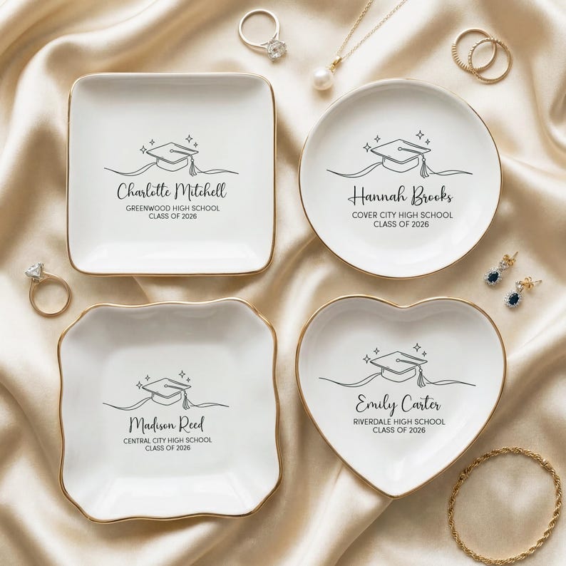May include: Four white ceramic trinket dishes with gold rims, each featuring a graduation cap design and a name with school details. The dishes are square, round, and heart-shaped, with text that reads "Charlotte Mitchell", "Hannah Brooks", "Madison Reed", and "Emily Carter".