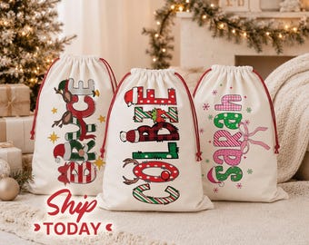 May include: Three off-white fabric drawstring bags featuring personalized names in festive patterns. The first bag displays the name BRUCE with reindeer and Santa hat accents. The second bag shows COLBIE with plaid and holiday motifs. The third bag features SARAH with pink leopard print and a bow.