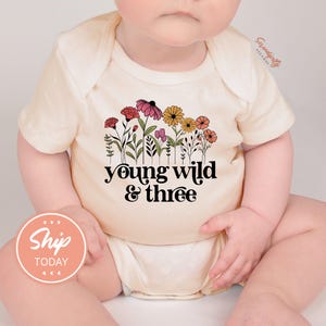 a baby wearing a shirt that says young wild and three