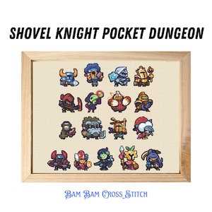 May include: A framed cross-stitch pattern featuring characters from the Shovel Knight Pocket Dungeon video game. The characters are depicted in a pixelated style and include Shovel Knight, Shield Knight, and others. The frame is made of wood and has a light brown finish. The text "BAM BAM CROSS STITCH" is printed below the image.