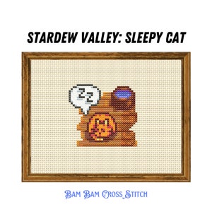 May include: Cross stitch pattern of a brown cat sleeping in a wooden cat bed with a blue water bowl. The cat has a speech bubble above its head with the letters "ZZ" inside. The pattern is framed in a brown wooden frame.