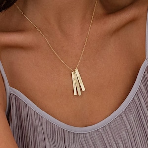 May include: A gold necklace with four vertical bar pendants. Each bar has a different name engraved on it.