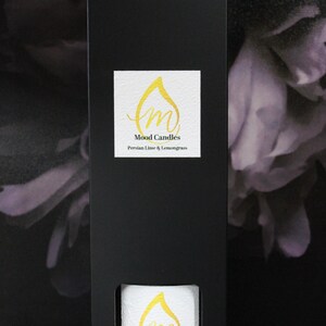 May include: A black box with a white label that says "Mood Candles" and "Persian Lime & Lemongrass". The box is sitting on a purple and white floral background.