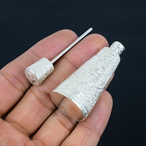 Puede incluir: Una botella de plata, de forma cónica y adornada, con un tapón de plata a juego. La botella tiene un intrincado diseño floral.