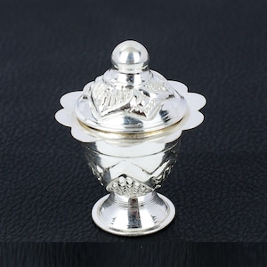 May include: A silver, ornate, decorative container with a lid. The container has a round base and a round lid with a finial. The container is decorated with intricate floral patterns.