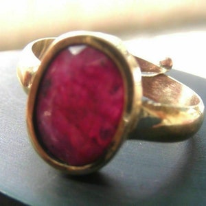 Può includere: Un anello d'oro con una grande pietra preziosa di rubino rosso scuro di forma ovale.