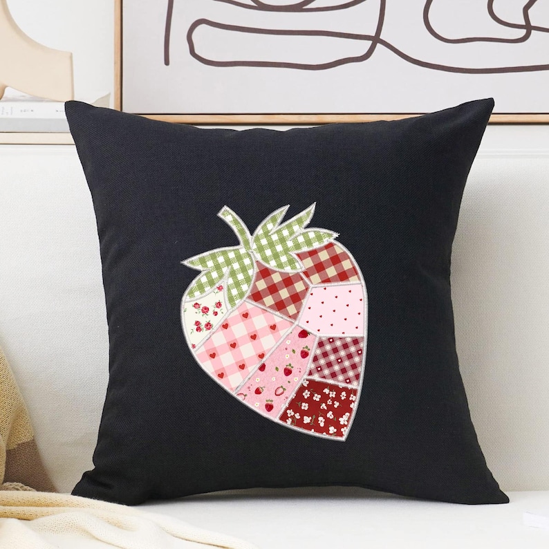 May include: Black square throw pillow featuring a patchwork strawberry design. The strawberry is composed of various fabric patterns, including gingham, polka dots, and floral prints in shades of red, pink, and green. The pillow is a decorative home accent.