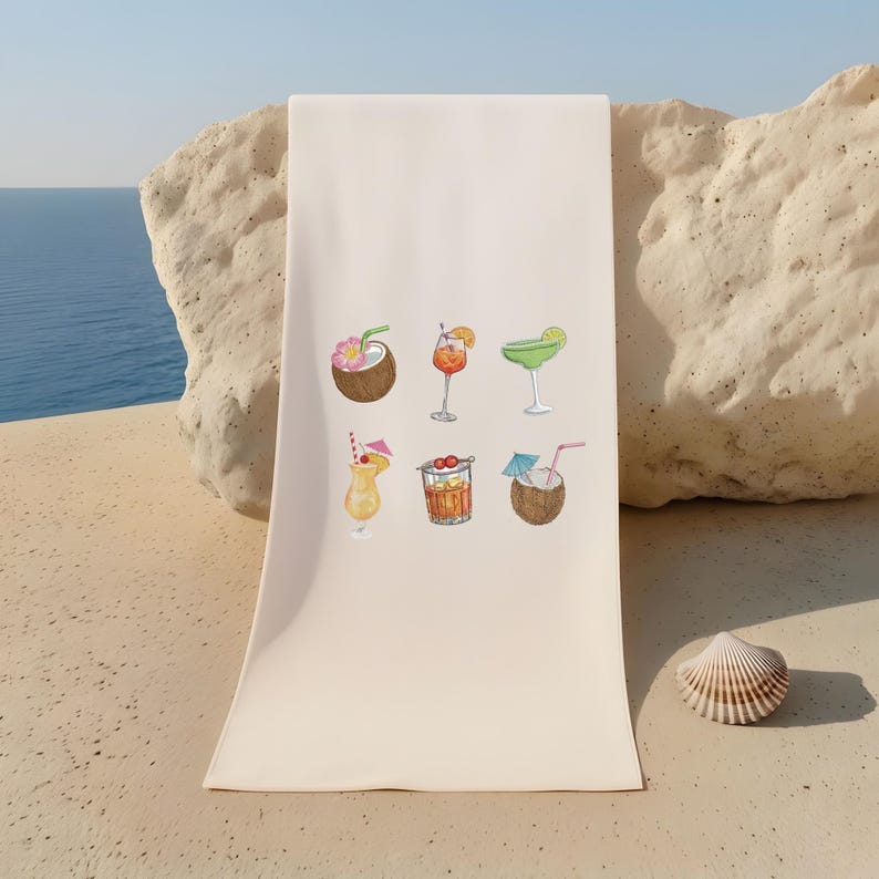 May include: A cream-colored beach towel featuring watercolor illustrations of six tropical cocktails. The drinks include a coconut with a flower, a cocktail in a stemmed glass with an orange slice, and a margarita with a lime wedge.