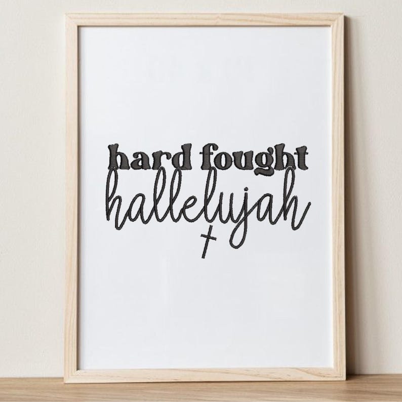 K&ouml;nnte beinhalten: Gerahmter Druck mit den Worten "hard fought hallelujah" in schwarzer Schrift und einem kleinen Kreuz. Die Worte sind auf wei&szlig;em Hintergrund zentriert, der Rahmen ist helles Holz.