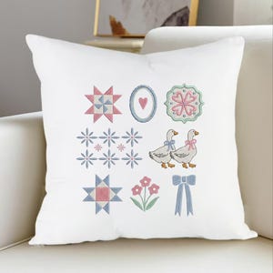 May include: White decorative pillow with embroidered designs. Features include geometric shapes, floral patterns, and two geese with bows. The color palette includes pink, blue, and green accents, creating a charming, country-inspired aesthetic.