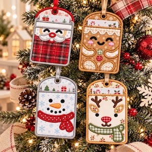 May include: Four rectangular fabric gift card holders hanging as ornaments. One features a Santa face with red plaid, one a gingerbread person, one a snowman with a red scarf, and one a reindeer with a green scarf, all with festive details.