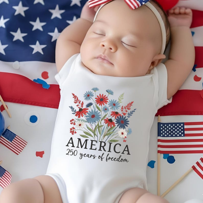 Puede incluir: Un body blanco para beb&eacute; con un dise&ntilde;o floral en rojo, blanco y azul, con la palabra "AMERICA" y "250 years of freedom" impresas debajo. El beb&eacute; est&aacute; acostado sobre una bandera estadounidense.