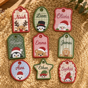 Puede incluir: Nueve etiquetas de regalo de tela bordada en varias formas con personajes navideños y nombres. Las etiquetas muestran a Noah, Liam, Olivia, Mason, Emma, James, Ava, Ethan y Sophia junto a iconos como un reno, muñeco de nieve, Santa, pingüino, oso, hombre de jengibre, oso polar, elfo y ratón.