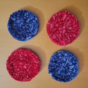 Puede incluir: Cuatro posavasos redondos de tela afelpada y texturizada. Dos son de un rojo vibrante y dos de un azul profundo. Los posavasos están dispuestos en un patrón cuadrado, ofreciendo un acento suave y colorido para cualquier decoración del hogar.