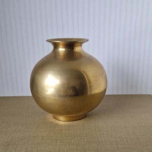 Puede incluir: Un jarrón pequeño, redondo, de latón de color dorado con un borde ligeramente acampanado.