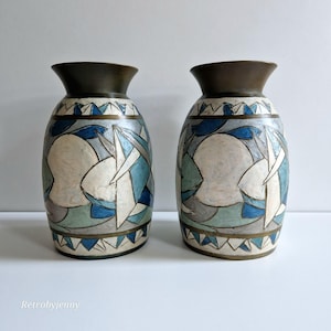 Puede incluir: Un par de jarrones de cerámica con un diseño geométrico en tonos azules, blancos y dorados. Los jarrones tienen una forma redondeada y una boca ancha.