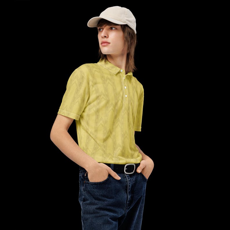 May include: A light yellow short-sleeved polo shirt with a subtle vertical chevron pattern, featuring a buttoned placket, paired with dark blue denim jeans, a black belt with a silver buckle, and a plain light-colored baseball cap.
