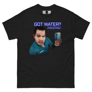 May include: A black short-sleeve t-shirt featuring a graphic of a person in a blue jacket holding a blue can. The text reads GOT WATER? and They put something in it, to make you smarter... The shirt has a small rectangular label at the neckline.