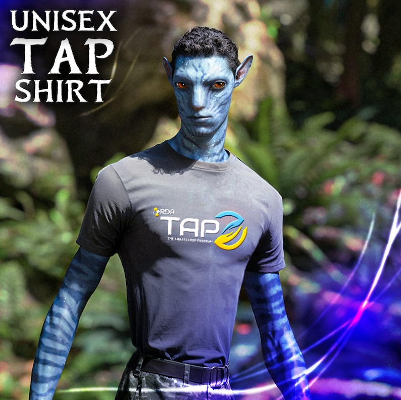May include: A blue-skinned person wearing a gray t-shirt with the text "RDA TAP THE AMBASSADOR PROGRAM" printed on the front. The person is standing in front of a blurred background of green foliage.