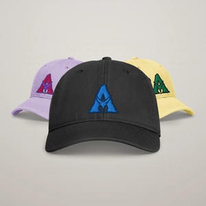 May include: Three baseball caps in black, light purple, and pale yellow. The black cap features a blue embroidered letter A with a central icon. The purple cap has a red embroidered letter A, and the yellow cap has a green embroidered letter A.