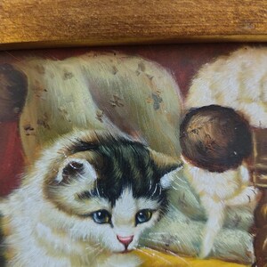 May include: A painting of two white and gray kittens sitting on a yellow chair. The kitten in the foreground is looking down with blue eyes. The background is a dark red color.