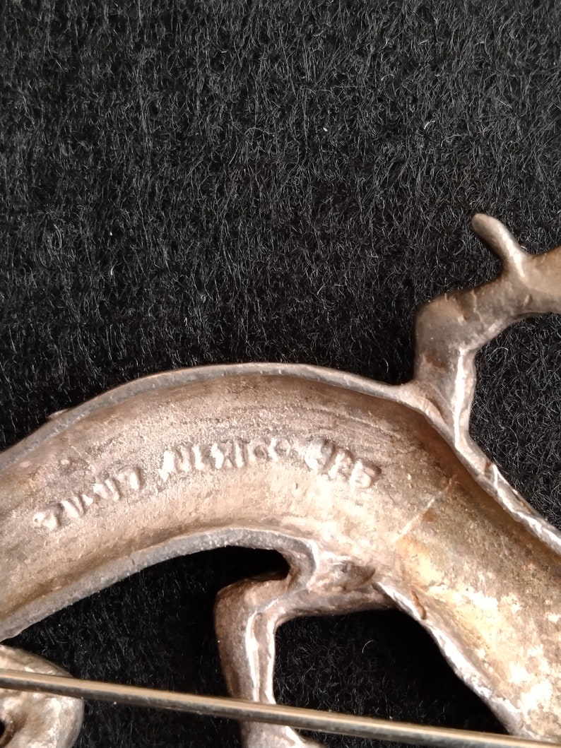 Op de afbeelding: Zilverkleurige metalen broche met een gestileerd springend hert. De achterkant van de broche is gemarkeerd met "Hand Wrought."